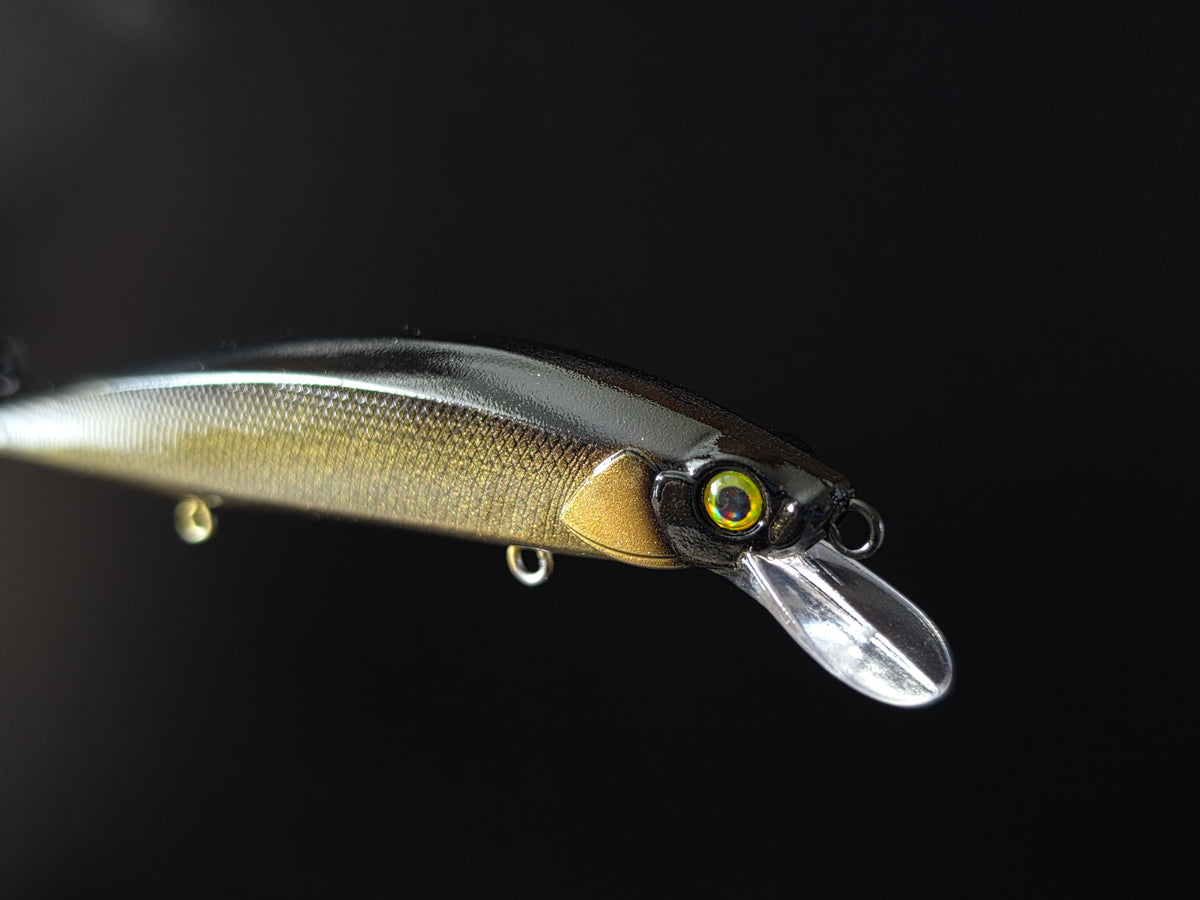 A close-up of a hard fishing lure with a clear diving lip, a black top, and a gold-tan underside, shown against a solid black background.