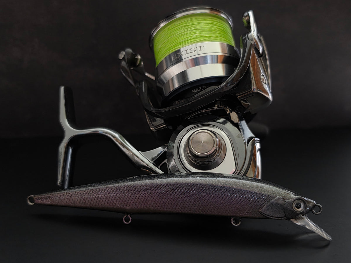A spinning fishing reel with bright green line spool mounted above a purple and black bait lure, photographed on a dark studio background.