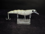 A white and translucent hard bait fishing lure with 2 treble hooks, displayed on a clear acrylic stand against a dark background.