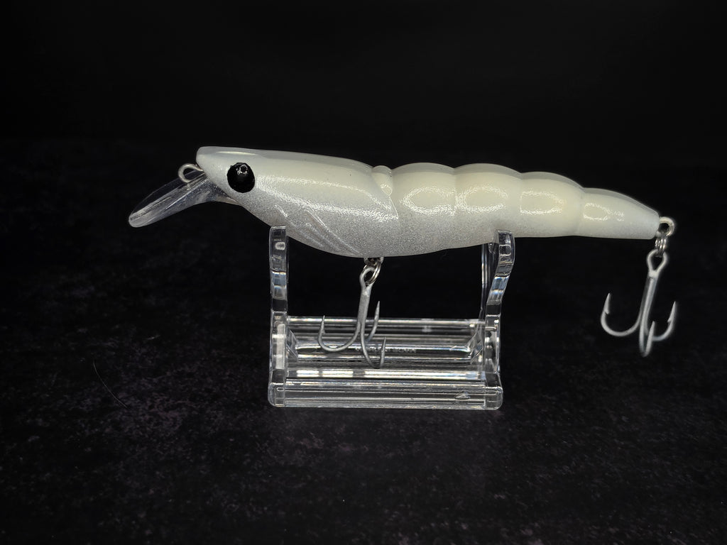 A white hard bait fishing lure with a clear diving lip and metal treble hooks, displayed on a clear acrylic stand against a black background.