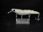 A white hard bait fishing lure with a clear diving lip and metal treble hooks, displayed on a clear acrylic stand against a black background.