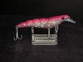 A pink and iridescent fishing lure with two treble hooks, displayed on a clear acrylic stand against a black background.