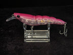 A pink translucent hard bait fishing lure with a clear plastic diving bill and treble hooks, displayed on a clear acrylic stand against a black background.