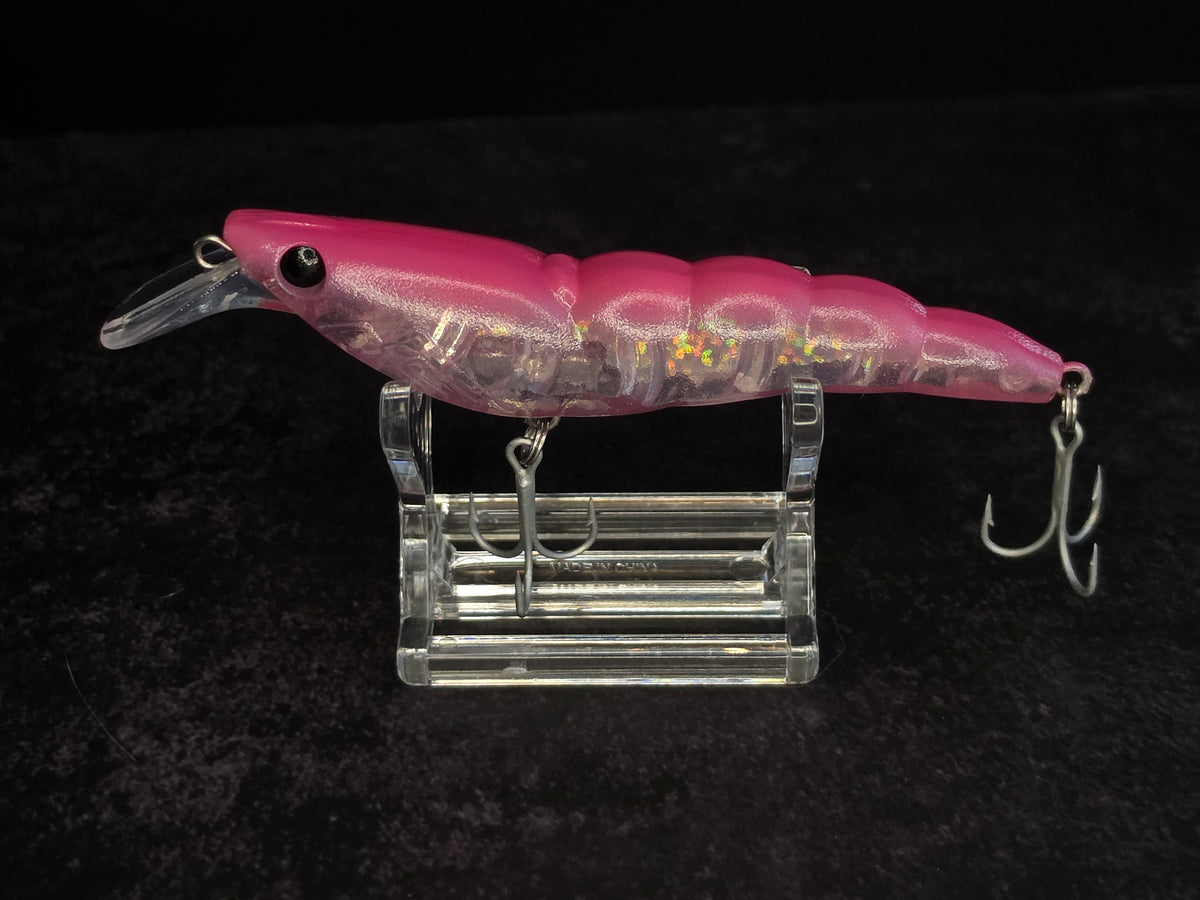 A pink translucent hard bait fishing lure with a clear plastic diving bill and treble hooks, displayed on a clear acrylic stand against a black background.