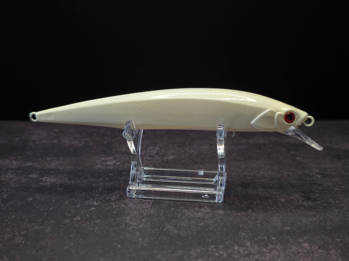A cream-colored hard fishing lure with a red eye and clear diving lip, displayed on a clear acrylic stand against a dark background.