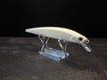 A white hard bait fishing lure with a clear diving lip and red eye, displayed on a transparent acrylic stand against a dark background.
