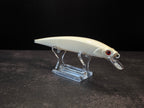 A white hard bait fishing lure with a clear diving lip and red eye, displayed on a transparent acrylic stand against a dark background.