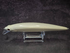 A cream-colored hard fishing lure with a textured scale pattern, resting on a clear acrylic stand against a dark textured background.
