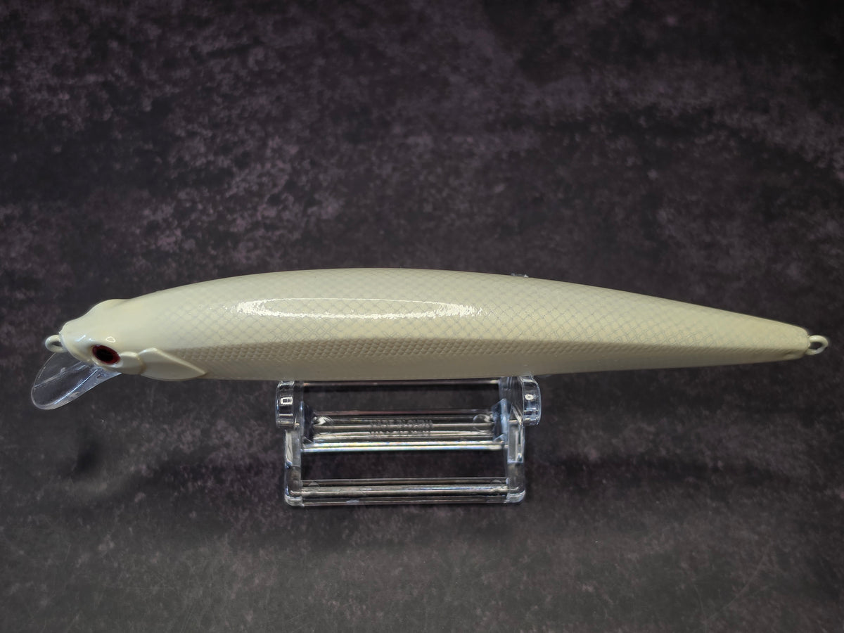 A cream-colored hard fishing lure with a textured scale pattern, resting on a clear acrylic stand against a dark textured background.