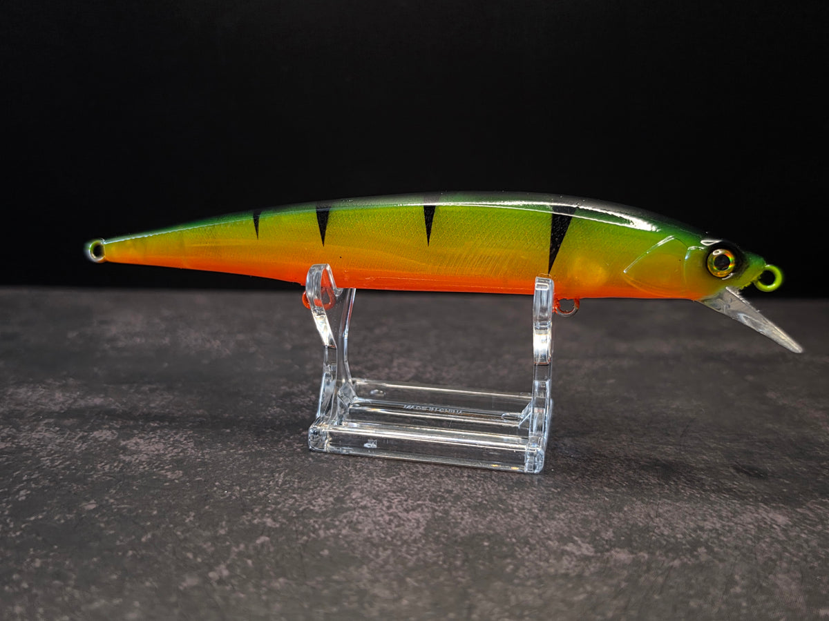 A hard bait fishing lure with a yellow-to-orange gradient body, black vertical stripes, and a clear diving lip, displayed on a clear acrylic stand against a dark background.