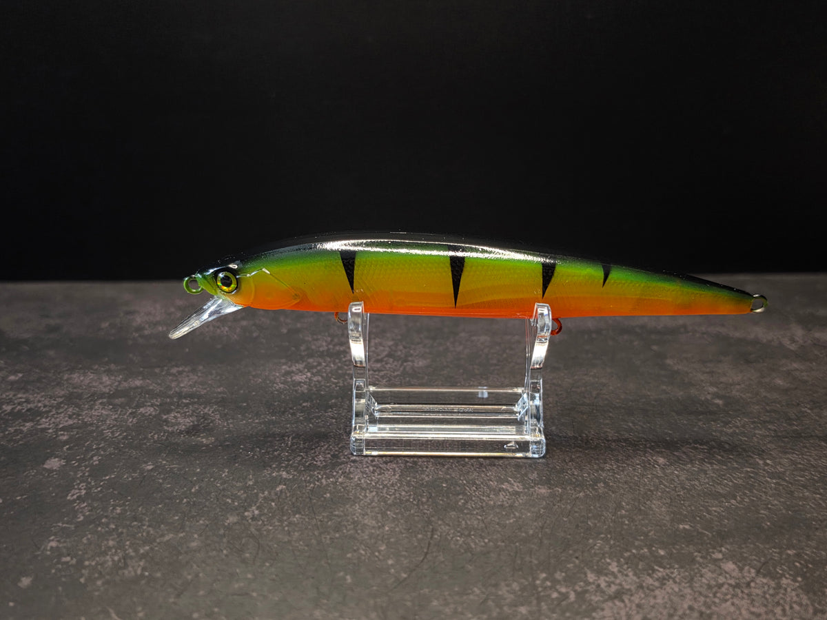 A hard bait fishing lure with a green, yellow, and orange tiger-stripe pattern, mounted on a clear acrylic stand against a dark background.