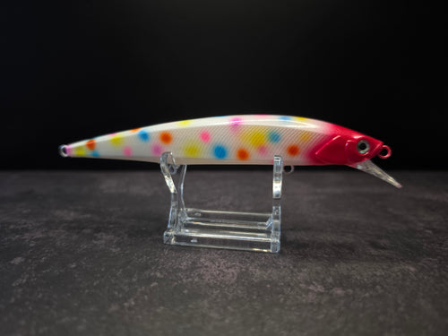 A hard bait fishing lure with a white body covered in colorful polka dots, featuring a bright red head and a clear plastic diving lip, displayed on a clear acrylic stand against a dark background.