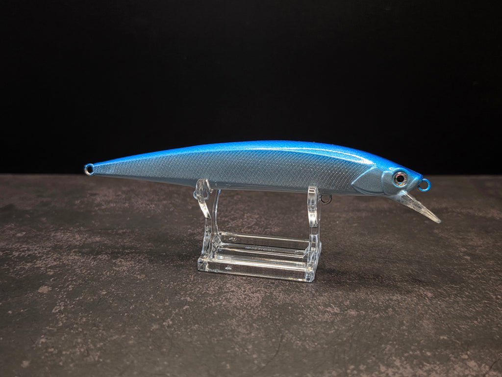 A blue and silver hard bait fishing lure with a clear plastic diving lip, displayed on a transparent acrylic stand against a dark background.