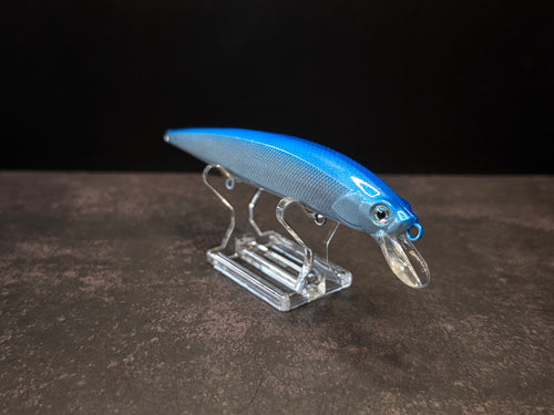 A blue and silver crankbait fishing lure with a clear plastic diving lip, displayed on a clear acrylic stand against a dark background.