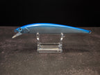 A blue and silver hard bait fishing lure with a clear plastic diving lip, displayed on a clear acrylic stand against a dark background.