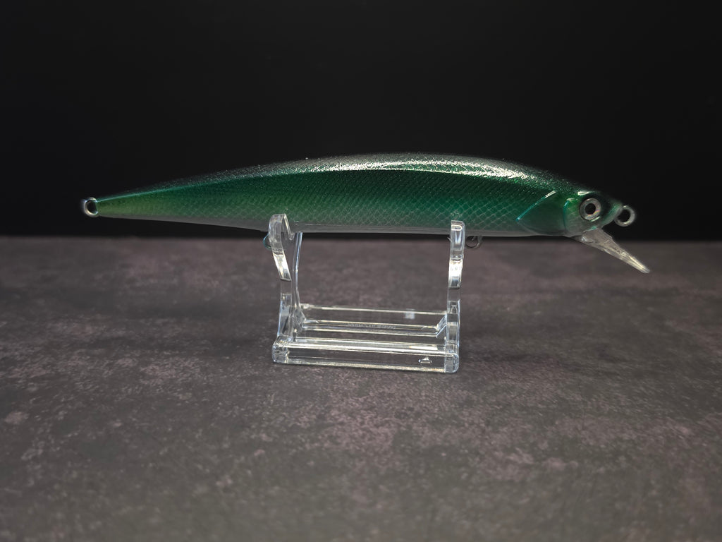 A green metallic fishing lure with a clear plastic diving lip, displayed on a clear acrylic stand against a dark background.