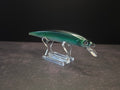 A metallic green and black hard bait fishing lure with a clear plastic lip, displayed on a clear acrylic stand against a dark background.