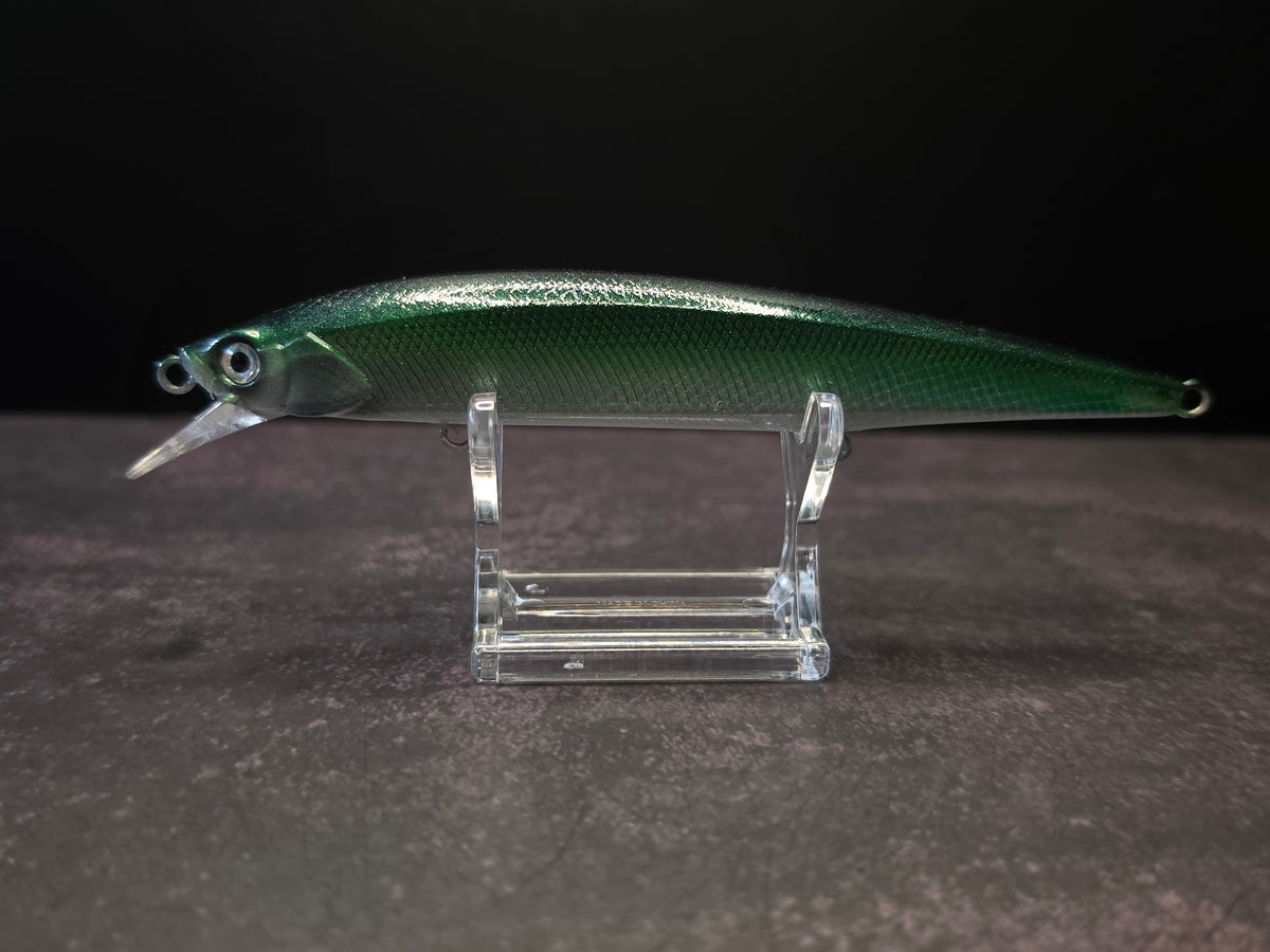 A green metallic fishing lure with a clear plastic diving lip, displayed on a clear acrylic stand against a dark background.