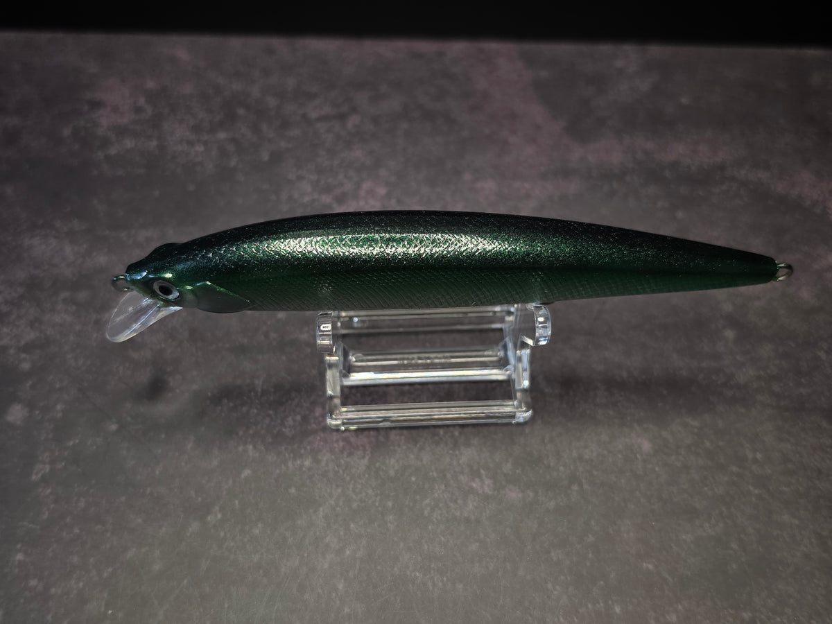 A metallic dark green fishing lure with a clear diving lip, displayed on a clear acrylic stand against a textured gray background.