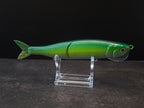 Dark green to light green gradient colored fish shaped moon bill glide bait on a clear acrylic stand against a black and gray background. 