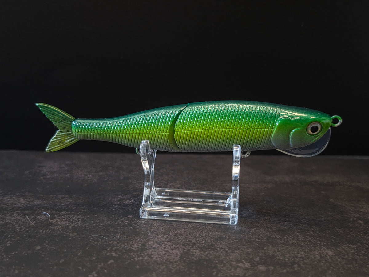 Dark green to light green gradient colored fish shaped moon bill glide bait on a clear acrylic stand against a black and gray background. 