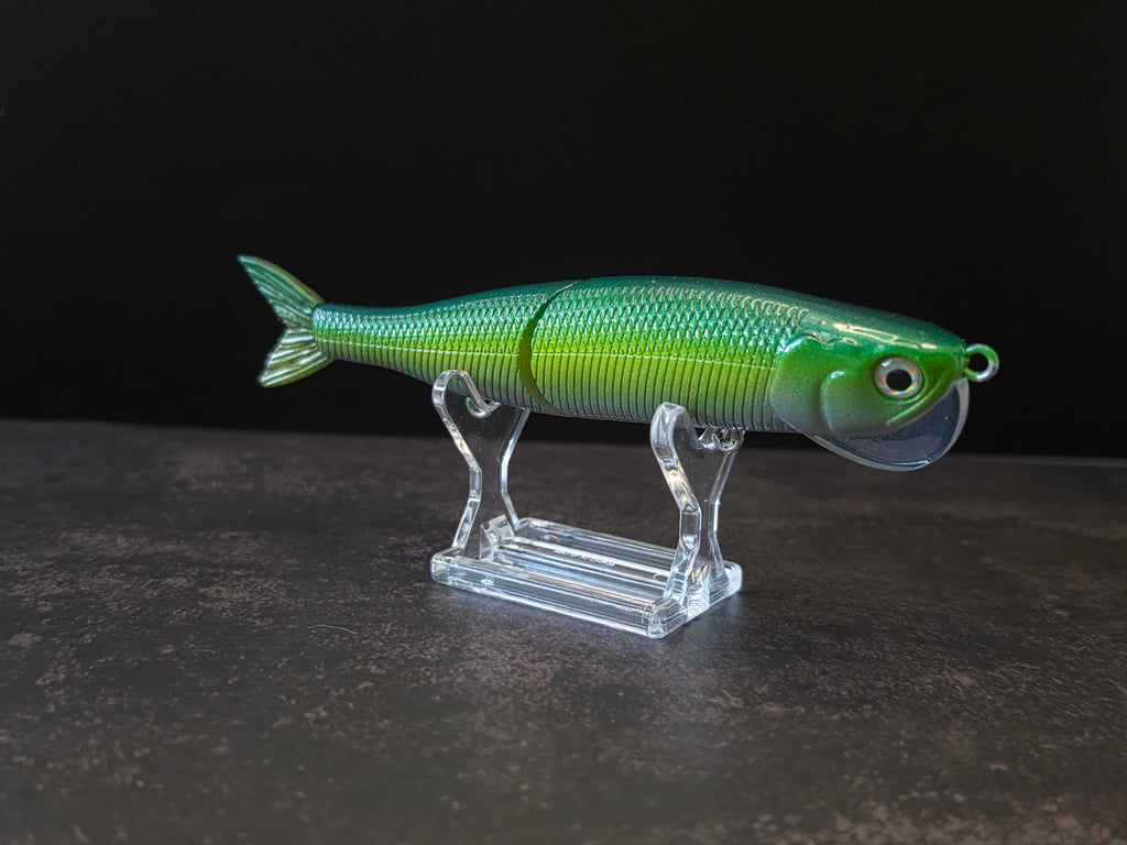 Dark green to light green gradient colored fish shaped moon bill glide bait on a clear acrylic stand against a black and gray background. 