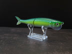 Dark green to light green gradient colored fish shaped moon bill glide bait on a clear acrylic stand against a black and gray background. 