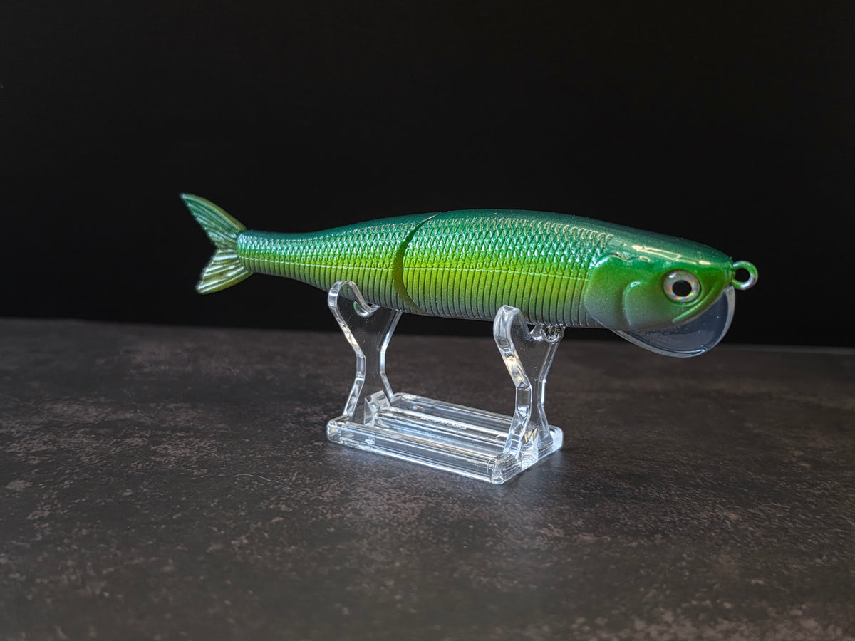 Dark green to light green gradient colored fish shaped moon bill glide bait on a clear acrylic stand against a black and gray background. 