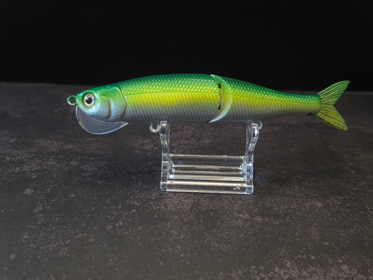 Dark green to light green gradient colored fish shaped moon bill glide bait on a clear acrylic stand against a black and gray background. 