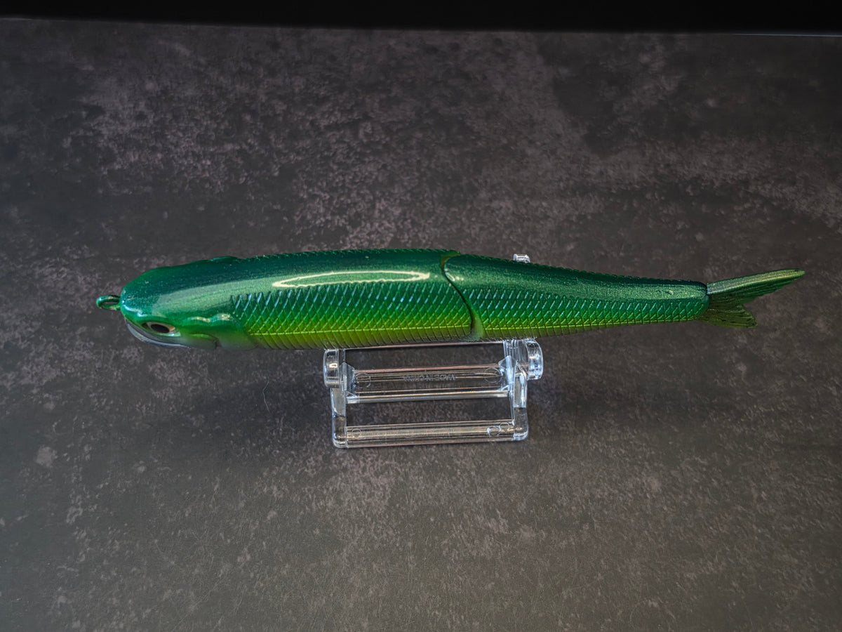 Dark green to light green gradient colored fish shaped moon bill glide bait on a clear acrylic stand against a black and gray background. 