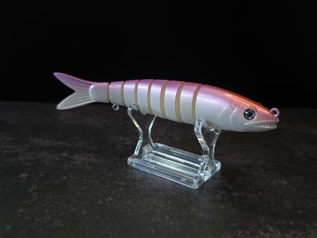 A pink and white gradient hard fishing lure shaped like a small fish, displayed on a clear acrylic stand against a dark background.