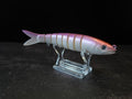 A pink and white gradient hard fishing lure shaped like a small fish, displayed on a clear acrylic stand against a dark background.