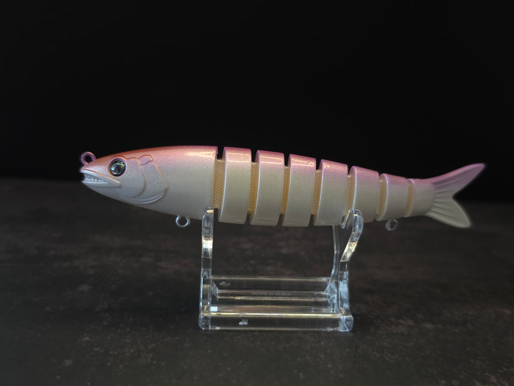 A pink and white gradient hard fishing lure shaped like a small fish, displayed on a clear acrylic stand against a dark background.