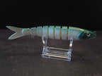 A hard plastic fishing lure shaped like a fish, featuring green to white gradient coloring with a green head, displayed on a clear acrylic stand against a dark background.