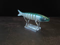 A hard plastic fishing lure shaped like a fish, featuring green to white gradient coloring with a green head, displayed on a clear acrylic stand against a dark background.