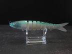 A hard plastic fishing lure shaped like a fish, featuring green to white gradient coloring with a green head, displayed on a clear acrylic stand against a dark background.