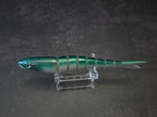 A hard plastic fishing lure shaped like a fish, featuring green to white gradient coloring with a green head, displayed on a clear acrylic stand against a dark background.