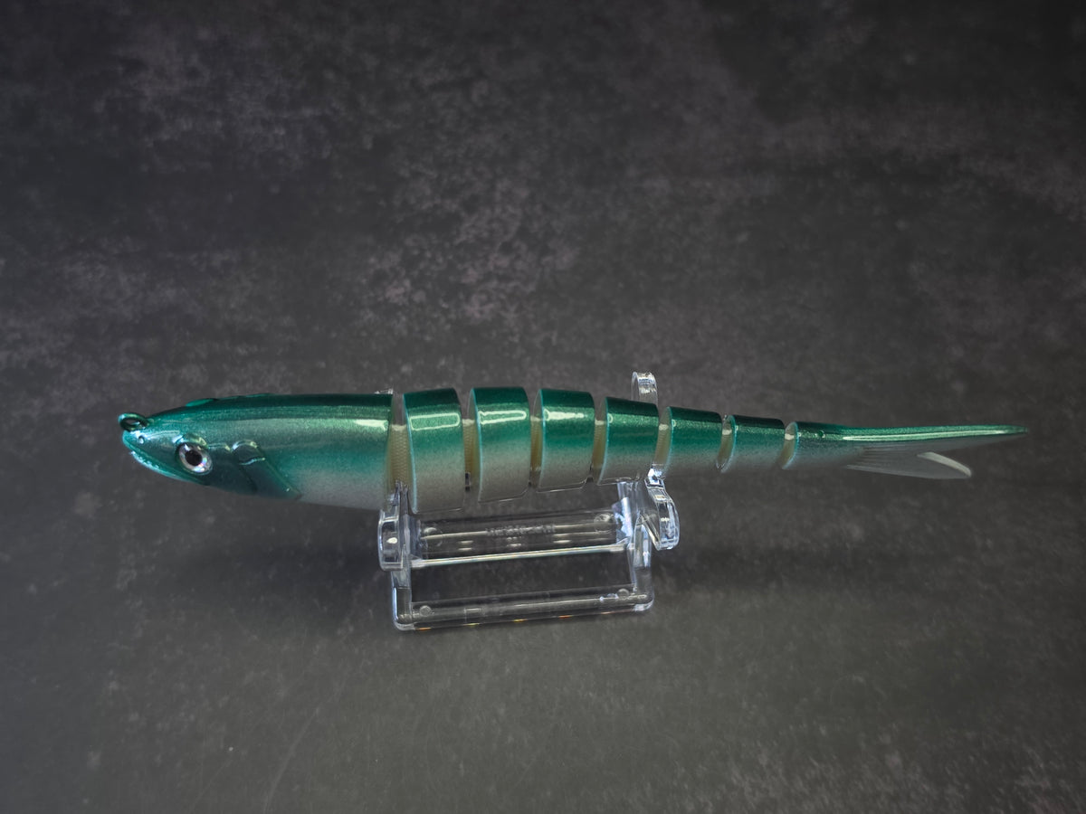 A hard plastic fishing lure shaped like a fish, featuring green to white gradient coloring with a green head, displayed on a clear acrylic stand against a dark background.